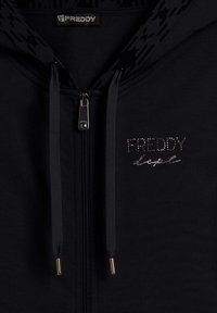 Felpa nera con zip e cappuccio testurizzato, caratterizzata da dettagli in argento e la scritta "FREDDY" in strass sul petto. Texture del tessuto liscia.
