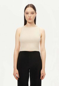 Beige ribbad ärmlös crop top med rund halsringning, b ärs med svarta ribbade hög midja-byxor. Slät tygtextur, figursydd design.