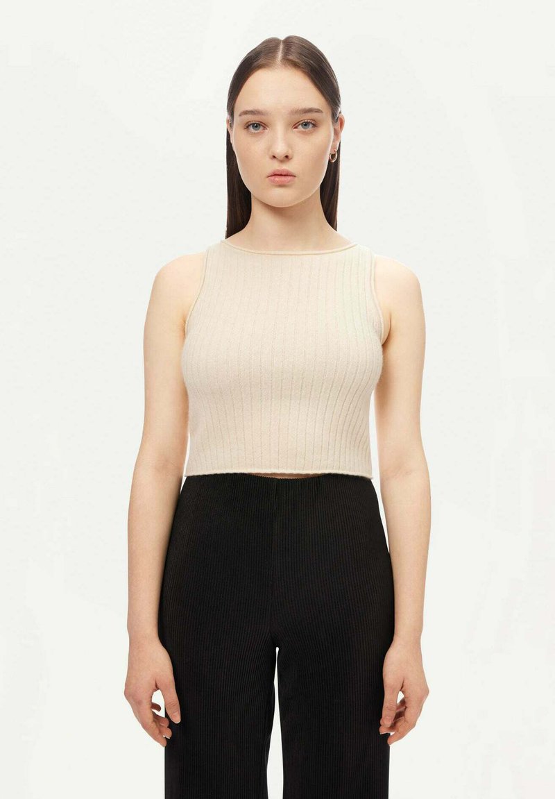 Beige ribbad ärmlös crop top med rund halsringning, bärs med svarta ribbade hög midja-byxor. Slät tygtextur, figursydd design.