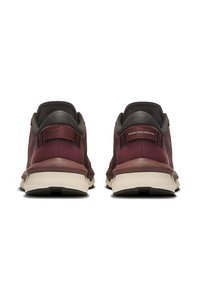 Røde og grå sportssko med en tekstureret overdel, polstret krave og hvid sål. Bagfra vises mærkets label og designkonturer.