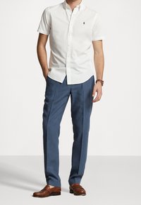 Camicia bianca a maniche corte con bottoni abbinata a pantaloni eleganti blu, caratterizzata da una vestibilità rilassata e mocassini in pelle marrone.