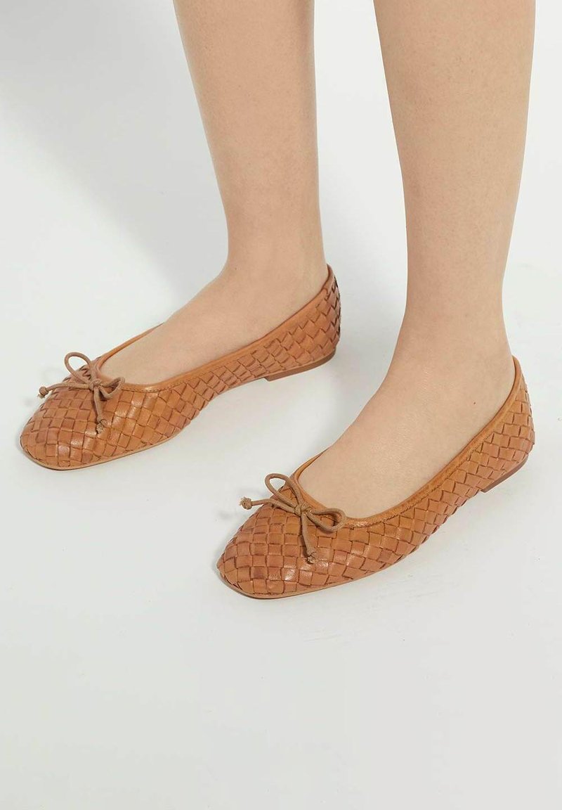 Vlechten van tan lederen balletschoenen met een ronde neus en een dunne strikdetails. Zachte textuur en flexibele constructie voor comfort.