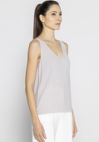 Jasnoróżowy bezrękawnik z dekoltem w kształcie litery V, wykonany z teksturowanej dzianiny, z luźnym krojem i prostym dołem. Połączony z białymi spodniami.