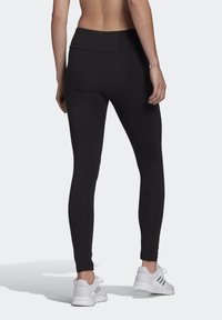 Svarta sportleggings med hög midja, slät textur och en åtsittande design, tillsammans med vita sportskor.