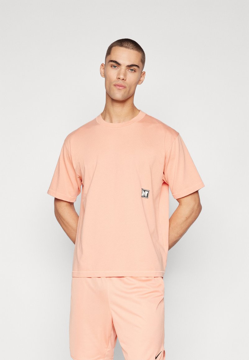 Tricou cu mânecă scurtă, de culoare roz pal, realizat din bumbac moale, având o mică patch cu logo alb și negru pe partea stângă a pieptului.
