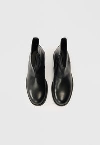 Juodi odiniai aulinukai suapvalintu priekiu, lygiu paviršiumi, šoninėmis užtrauktukais ir plokščia gumine padais. Be matomų raštų ar akcentų.