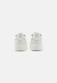 White leather sneakers with a chunky sole, featuring a back tab and embossed branding on the heel. Smooth texture with minimalistic design.