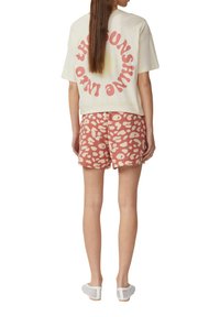 Gekürztes cremfarbenes T-Shirt mit pinkem Grafikdruck, kombiniert mit pink-weißen gepunkteten Shorts. Das Modell trägt weiße Mesh-Slips.
