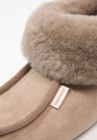 Beige suede slipper featuring a soft, fluffy brown shearling cuff, brown laces, and a white label with "SHEPHERD" in orange text.
