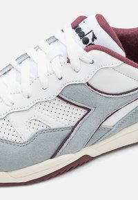 Hvit og grå atletisk sneakers med semsket tekstur, perforerte detaljer, burgunder aksenter og flate hvite snører. Merkbar logo på tungen.