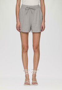 Lichtgrijze shorts van gestructureerde stof met een elastische tailleband en een strikdetail. Gepaard met witte sandaaltjes met bandjes.