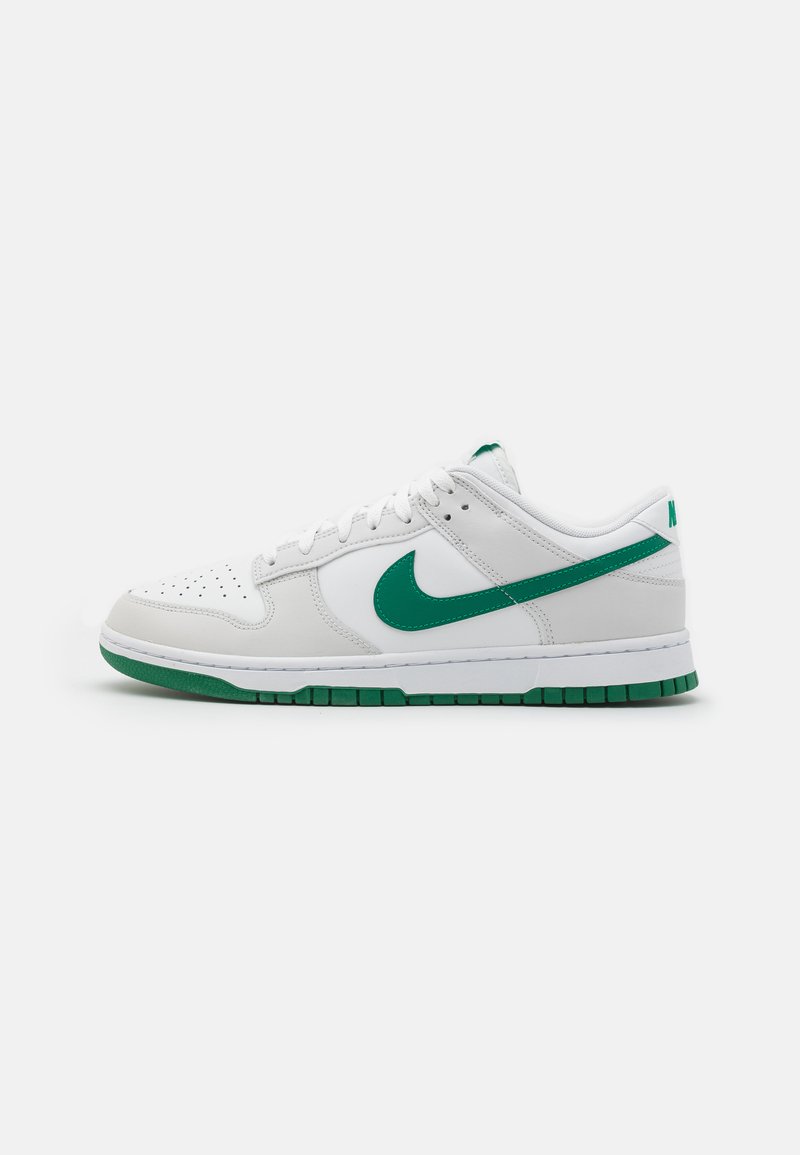 Tênis Nike brancos com detalhes verdes, apresentando um cabedal em couro liso, caixa de ponta perfurada e uma sola de borracha com padrão estriado.