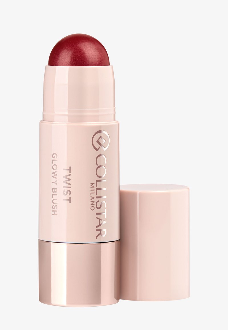 Stick de blush rétractable dans un emballage rose pâle, avec une pointe ronde et scintillante de couleur rouge foncé. Orné du logo de la marque et du nom du produit.