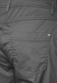 Gros plan sur l'arrière d'un pantalon gris foncé, centré sur une seule poche arrière avec des coutures visibles et un rivet dans le coin.