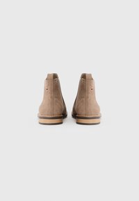 Botas de tobillo de ante marrón con un tacón bajo, paneles laterales elásticos y un pequeño acento tricolor cerca del tacón.