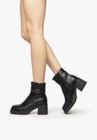 Black leather ankle boots with a chunky heel, featuring a buckle accent and a side zipper, on a plain white background.