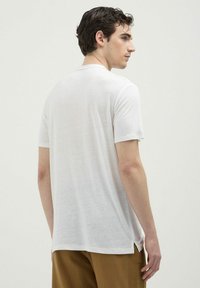 T-shirt bianco a maniche corte realizzato in tessuto morbido, con un taglio classico e una vestibilità comoda, completo di spacchi laterali per facilitare i movimenti.