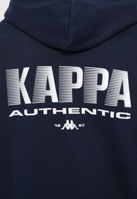 Temno modra kapuca z belim besedilom "KAPPA AUTHENTIC" in logotipom moškega in ženske, ki sedita hrbtno. Pod njima je napisano "1967".