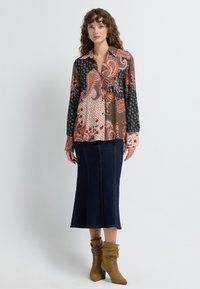 Multicolored patterned blouse with floral and geometric designs, paired with a dark denim skirt and tan slouchy ankle boots.
