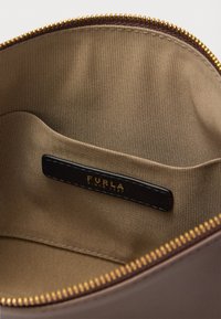 Barna bőrtáska belseje sima textil béléssel, arany cipzárzárral és egy fekete címkével, amelyen a "FURLA SINCE 1927" felirat dombornyomott.