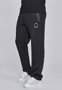 Crne sportske hlače s elegantnim dizajnom, s malim izvezenim logom, bočnim džepovima i patent-zatvaračima na gležnjevima za dodatnu funkcionalnost.