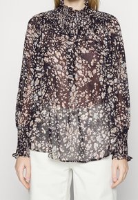 Blouse noire transparente avec un col haut froncé, des manches longues et un motif multicolore en taches de beige et bleu. Tissu doux et léger.