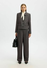 Harmaa räätälöity puku, jossa on lyhyt takki, kaksi etutaskua ja mustat napit. Yhdistetty leveälahkeisiin housuihin ja valkoiseen puseroon, jossa on rusetinauha.