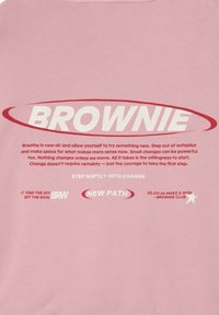 Sudadera rosa claro con texto audaz en blanco y rojo, con frases que promueven el cambio y la alegría. Incluye un gráfico de estrella y pequeños detalles.