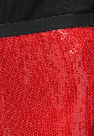 Tissu en sequins rouge avec une surface texturée, arborant une taille noire sur le dessus. Les sequins réfléchissent la lumière, créant un effet scintillant.