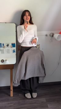 Grå oversized sweatshirt hænger på en hvid bøjle; brugt med løse mørke bukser og lyse, beige sneakers. Hvid bluse med lange ærmer under.