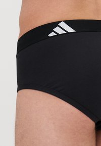 Schlichte schwarze Baumwollmischung Slips mit einem schwarzen Bund und drei weißen adidas Streifen auf der linken Seite. Glatte Textur, figurbetontes Design.
