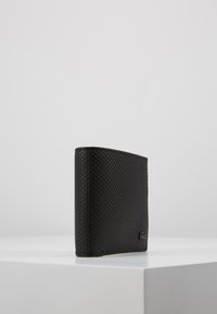 Μαύρο υφασμάτινο πορτοφόλι σε ορθογώνιο σχήμα, με λείο άνω άκρο και μινιμαλιστικό σχέδιο, τοποθετημένο σε λευκή επιφάνεια.