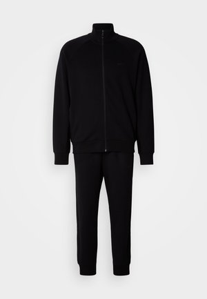 Black athletic tracksuit with a zip-up jacket and matching pants. Jacket features raglan sleeves; pants have elasticated cuffs and minimal branding.