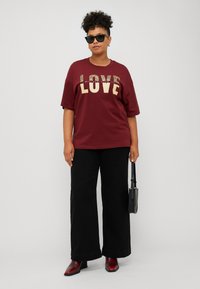 Maroon t-shirt with "LOVE" in gold glitter, black wide-leg pants, and red ankle boots. Black sunglasses and small black handbag as accessories.
