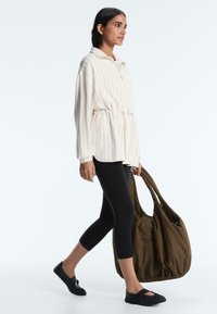 Ženska, ki hodi, oblečena v kremno jopico z ozkimi črtami, črne skrajšane legice, črne copate ter nosi veliko rjavo torbo tote.