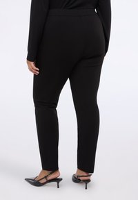 Černé elastické kalhoty se slim fit střihem, s vysokým pasem a hladkým povrchem, spárované s černými lodičkami na podpatku.