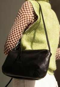 Borsa a tracolla in pelle nera con forma curva, superficie testurizzata e una sottile tracolla. Presenta un brand discreto sul davanti.