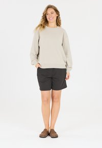 Ljusgrå sweatshirt med sänkta axlar, i kombination med svarta shorts och bruna slip-on skor, med en avslappnad passform och sidofickor.