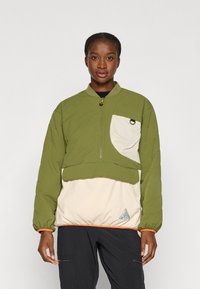 Chaqueta de cuadro verde con cuello alto, panel color crema en la parte delantera y puños elásticos. Presenta un acento naranja en el dobladillo.