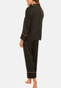 Ensemble de pyjama en soie noire avec un haut à boutons et un pantalon long, présentant des surpiqûres blanches aux poignets et au col, texture lisse et coupe décontractée.