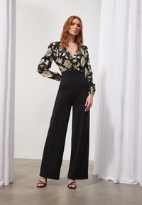 Pantalones de pierna ancha negros combinados con una blusa negra con patrones florales dorados. Tejido suave, diseño con escote en V y mangas abullonadas.
