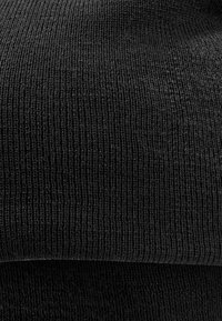 Material textil tricotat negru, cu o suprafață netedă și texturată și un model de nervuri constant, pliat la baza pentru un plus de adâncime.