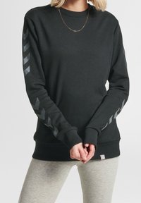 Sudadera negra con patrones de chevrones grises en las mangas, puños y dobladillo acanalados, y diseño de cuello redondo. Fabricada con un suave tejido texturizado.