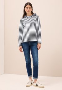 Sudadera de rayas azul marino y blanca con cuello de embudo, combinada con jeans azul con puños y zapatillas blancas con detalles en negro.