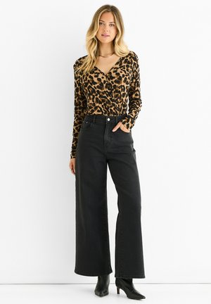 Langärmliges Oberteil mit Leopardenmuster, kombiniert mit hochtaillierten, weiten schwarzen Jeans und schwarzen Stiefeletten, aus glattem Material mit enganliegenden Ärmeln.