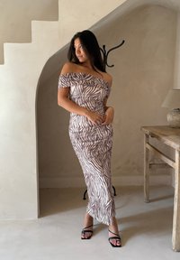 Rochie cu bretele căzute în tonuri de maro deschis, decorată cu dungi albe în stil zebra, având detalii drapate și o siluetă ajustată. Sandale negre cu barete.