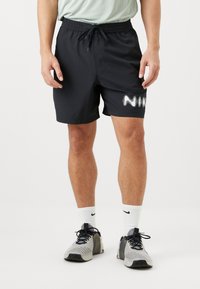 Pantaloni sportivi neri con elastico in vita e cordoncino, con il logo Nike bianco sul lato. Indossati con scarpe da ginnastica grigie e nere.