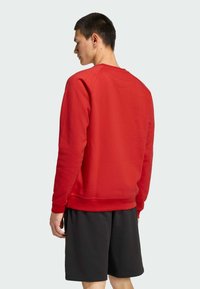 Crvena dukserica od pamuka s okruglim izrezom i rebrastim manžetama, u kombinaciji s crnim kratkim hlačama, prikazuje jednostavan, opušteni dizajn.