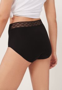 Sort bomuldsunderbukser med høj talje, der har en talje med blondetrimning og diamantmønster. Stoffet har en glat, mat tekstur.