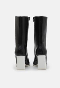 Botas de cuero negro hasta la rodilla con tacón cuadrado. Presentan una textura suave, cremalleras laterales y una base de tacón blanca en contraste.